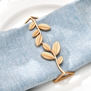 Detail of matte gold leaf napkin ring showing intricate veins on a light blue linen cloth