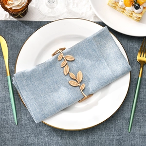 Detailed view of golden leaf napkin ring with intricate vein texture on a blue linen napkin