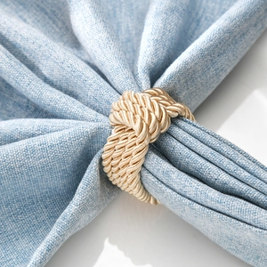Elegant hand-woven champagne gold knot napkin ring shown on a blue textured cloth