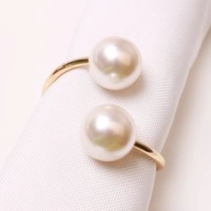 Elegant gold bypass napkin ring featuring two white pearls on a textured white background