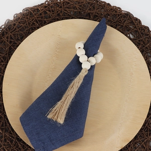 Rustic wooden bead napkin ring with natural jute tassel on a dark blue linen napkin