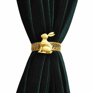 Detail of golden rabbit curtain tieback with flexible metal spring on green velvet drape