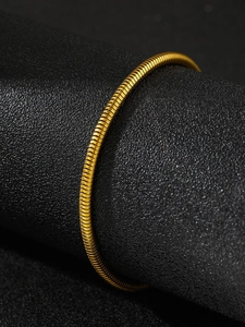 Macro close-up of a polished gold snake chain bracelet on a black leather stand