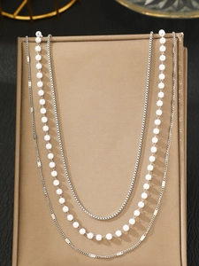 Detail of layered silver box chain and pearl necklace displayed on a jewelry stand