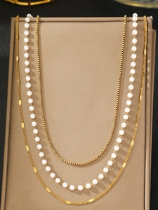 Detail of layered gold metal chain and white pearl strand on a brown jewelry display