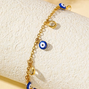 Chevillère dorée avec pendentif œil bleu et breloques en cristal sur un socle blanc texturé