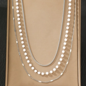 Three-layer layered necklace featuring pearls and silver chain on a display stand