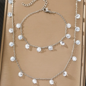 Polished silver necklace and bracelet set with round cubic zirconia on golden surface