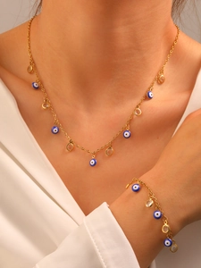 Detailed view of gold evil eye necklace and bracelet set worn on a white shirt