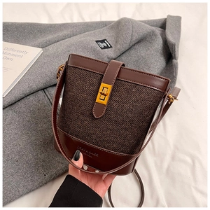 Detail of tweed and leather bucket bag with a golden turn-lock and embossed logo