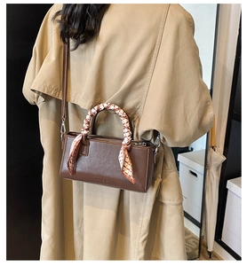 Bruine vintage handtas van kunstleer met decoratieve sjaal gedragen bij een trenchcoat