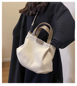 Detail view of cream canvas tote bag with khaki handles and adjustable crossbody strap