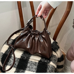 Close-up of glossy pleated brown leather handbag on a vintage wooden chair with strap detail