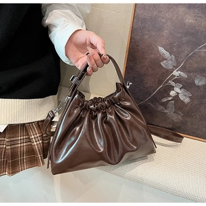 Detail of a brown pleated cloud bag made of premium glossy PU leather with silver hardware