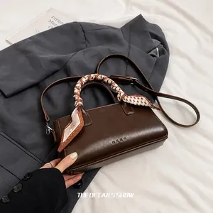 Detailed close-up of dark brown leather handbag with geometric pattern silk scarf on handle