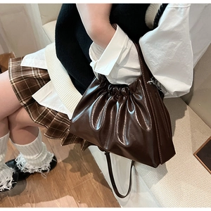 Detail of dark brown glossy pleated handbag featuring unique ruched handle and shoulder strap