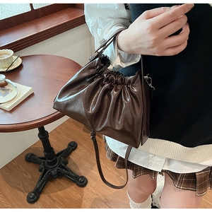 Close-up of a dark brown pleated cloud bag with shiny finish on a wooden cafe table