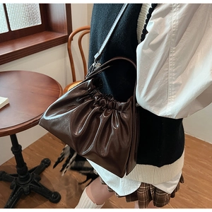 Detail of dark brown ruched cloud bag showing soft glossy leather texture and pleats