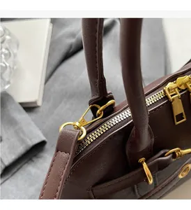 Detail of brown leather handbag featuring glossy gold hardware and precise stitching