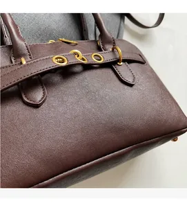 Close-up of brown textured leather handbag featuring golden metal rings and detailed stitching