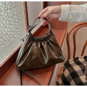 Detail of dark green pleated cloud bag featuring glossy texture and dual carry straps