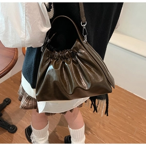 Detail of dark brown pleated cloud bag with glossy finish and detachable shoulder strap
