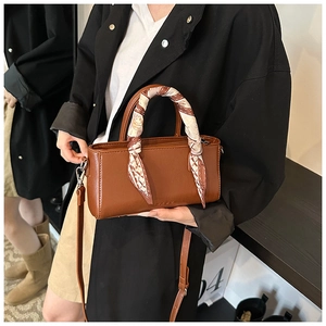 Detail van een bruine leren handtas met zijden sjaal en elegant reliëflogo op de tas