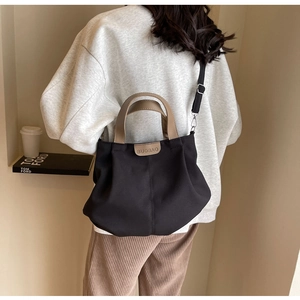 Detail of minimalist black canvas tote featuring brown leather handles and a versatile strap