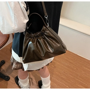 Brown pleated cloud bag with shiny PU leather texture shown in a lifestyle setting