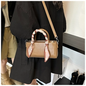 Detail van caramelbruine vierkante tas met zijden sjaal handvat en merklogo op tas