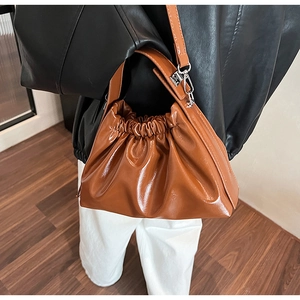 Detail view of a brown pleated cloud bag with glossy PU leather finish and thick handle