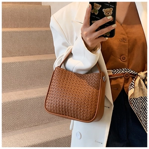Detail of a brown woven faux leather handbag with a minimalist semi-moon silhouette