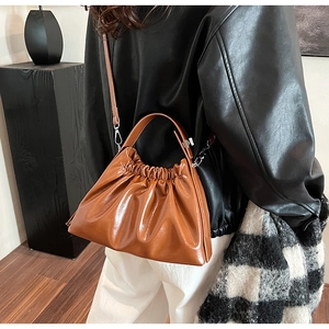 Detailed side view of brown pleated cloud bag with glossy texture on a model