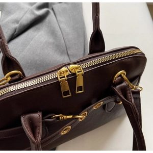 Detail shot of vintage gold dual zippers and leather texture on a dark brown handbag