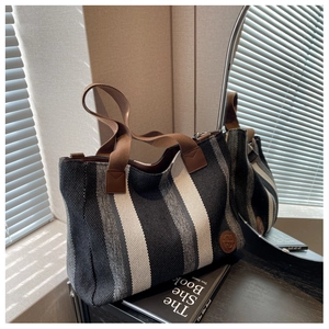 Detail of striped canvas tote bag with brown leather accents and circular logo on a desk