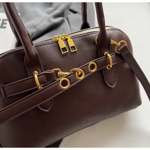 Close-up of deep brown leather bag showing dual gold zippers and metallic eyelet strap