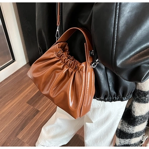 Brown glossy leather cloud bag with pleated design and silver hardware worn by a model
