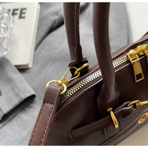 Close-up of golden dual-zipper closure and metal hardware on dark brown leather bag