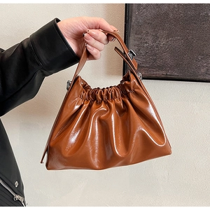 Detail shot of brown pleated cloud handbag with shiny leather finish and top handle