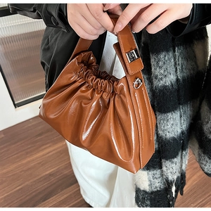 Detailed view of brown patent leather cloud bag with pleated design and silver buckle