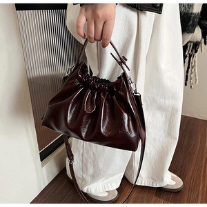 Close-up of a glossy dark brown pleated cloud bag featuring high-shine synthetic leather texture