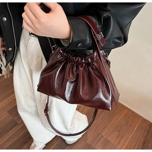 Detail of a dark red pleated cloud bag with glossy finish on a model wearing black leather