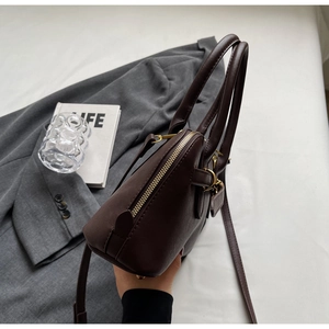 Detail of dark brown leather shell bag with gold hardware and smooth handle