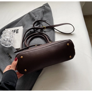 Detail of dark brown tote bag base with four protective gold metal feet and fine texture