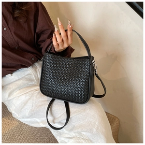Detail view of a black woven crossbody bag styled with professional outfit and metal buckle