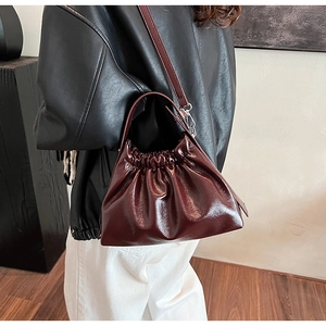 Detail shot of a glossy dark red ruched handbag with metallic finish and thin strap