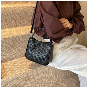 Close-up of black woven texture handbag with silver hardware on a neutral background