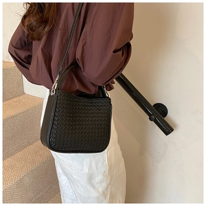 Close-up of a black woven crossbody bag with adjustable strap worn by a model