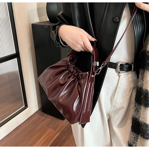 Close-up of glossy burgundy pleated handbag with adjustable shoulder strap and silver hardware