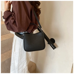 Fashionable black woven shoulder bag styled with an autumn outfit by the stairs